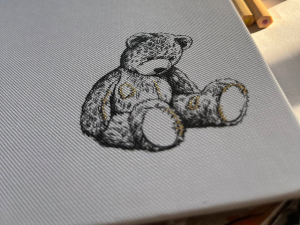 Close-up of a black-and-white illustrated teddy bear printed on the cloth cover of the children’s book Old Clothes, featuring metallic foil-stamped patch stitches on the bear’s paws and body.